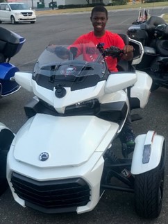 Teenage boy smiling and sitting inside a white 3-wheeled recreational vehicle.