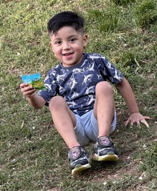 boy smiling, seated on grass hill.