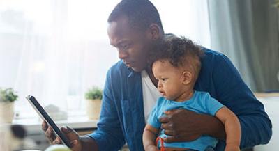 Parent holding a baby while looking at a tablet