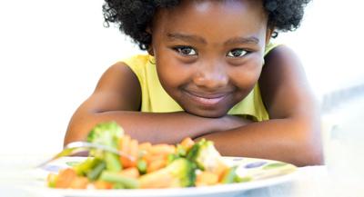 young girl smiling with plate of vegetables in front of her