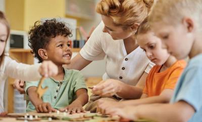 Boy sitting at table with other children and teacher, smiling.